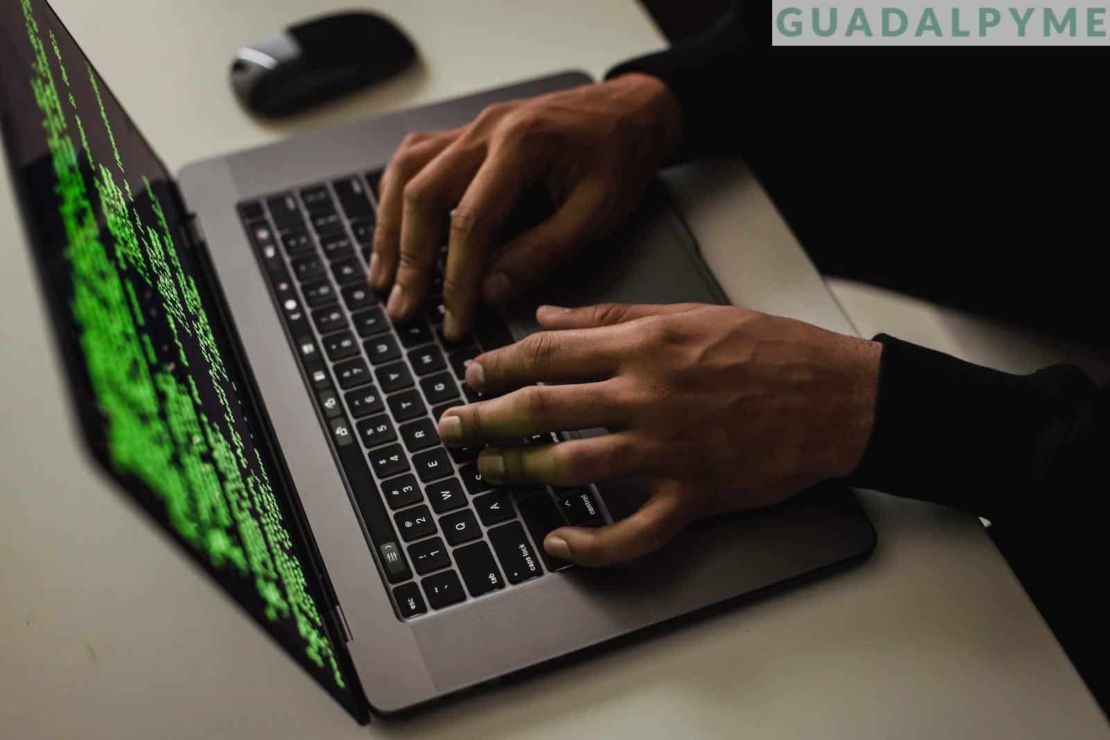 From above of crop anonymous male hacker typing on netbook with data on screen while sitting at desk